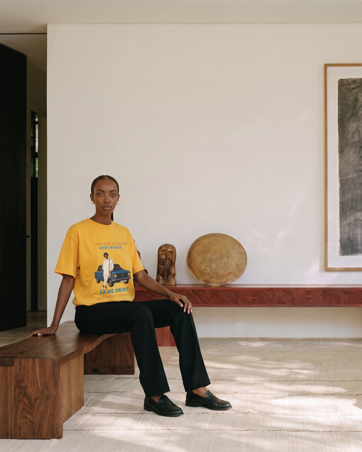 Model wearing the Addis in Blue tee in yellow, seated on a wooden bench